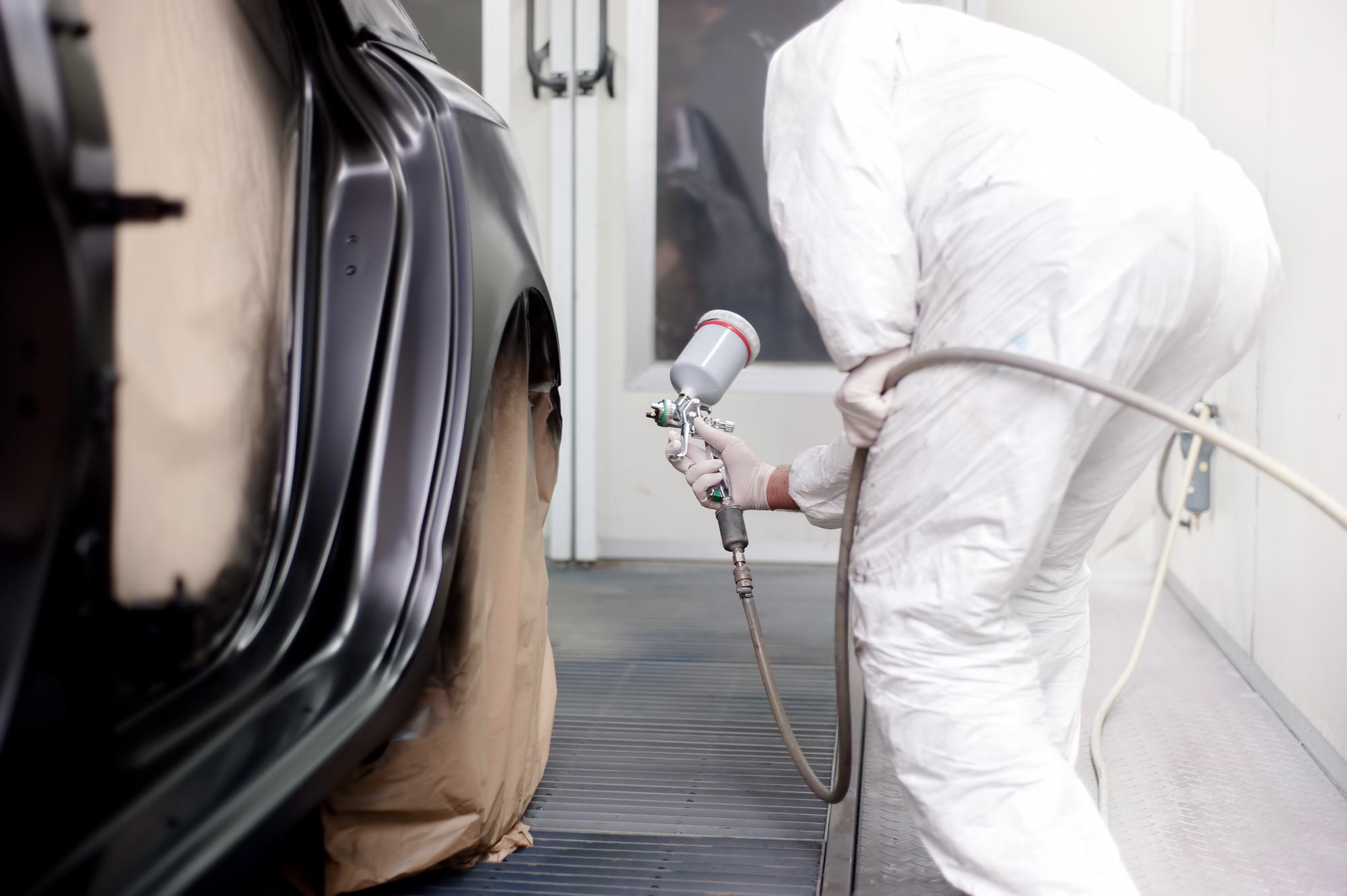 Vehicle engineer working and spraying black paint on a car in auto body shop